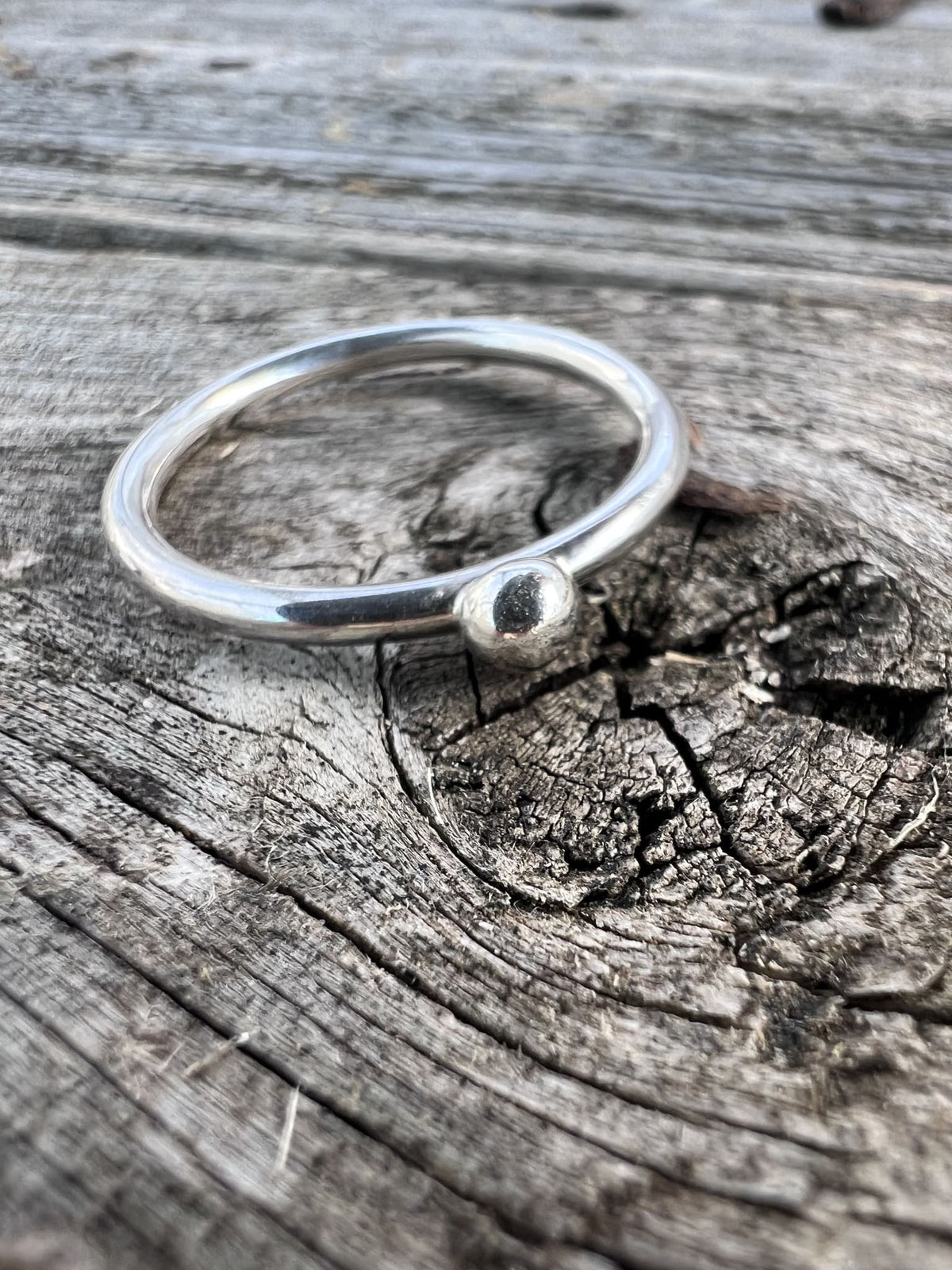 Recycled sterling silver single granule ring on driftwood, showing the fine band with a single silver granule detail