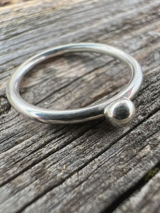 Close-up of a handmade sterling silver single granule ring on driftwood, highlighting the solitary fused silver bead