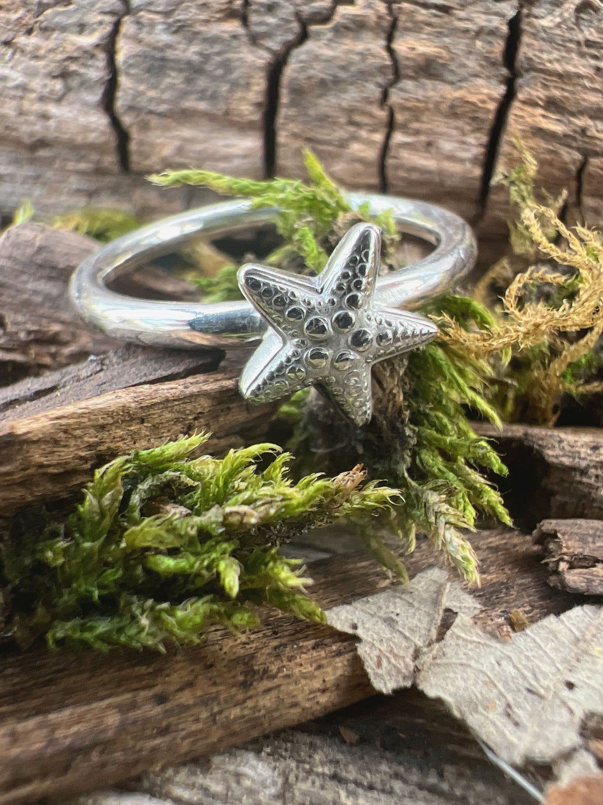 Handmade sterling silver small starfish ring on mossy driftwood, angled view showing the starfish in full relief