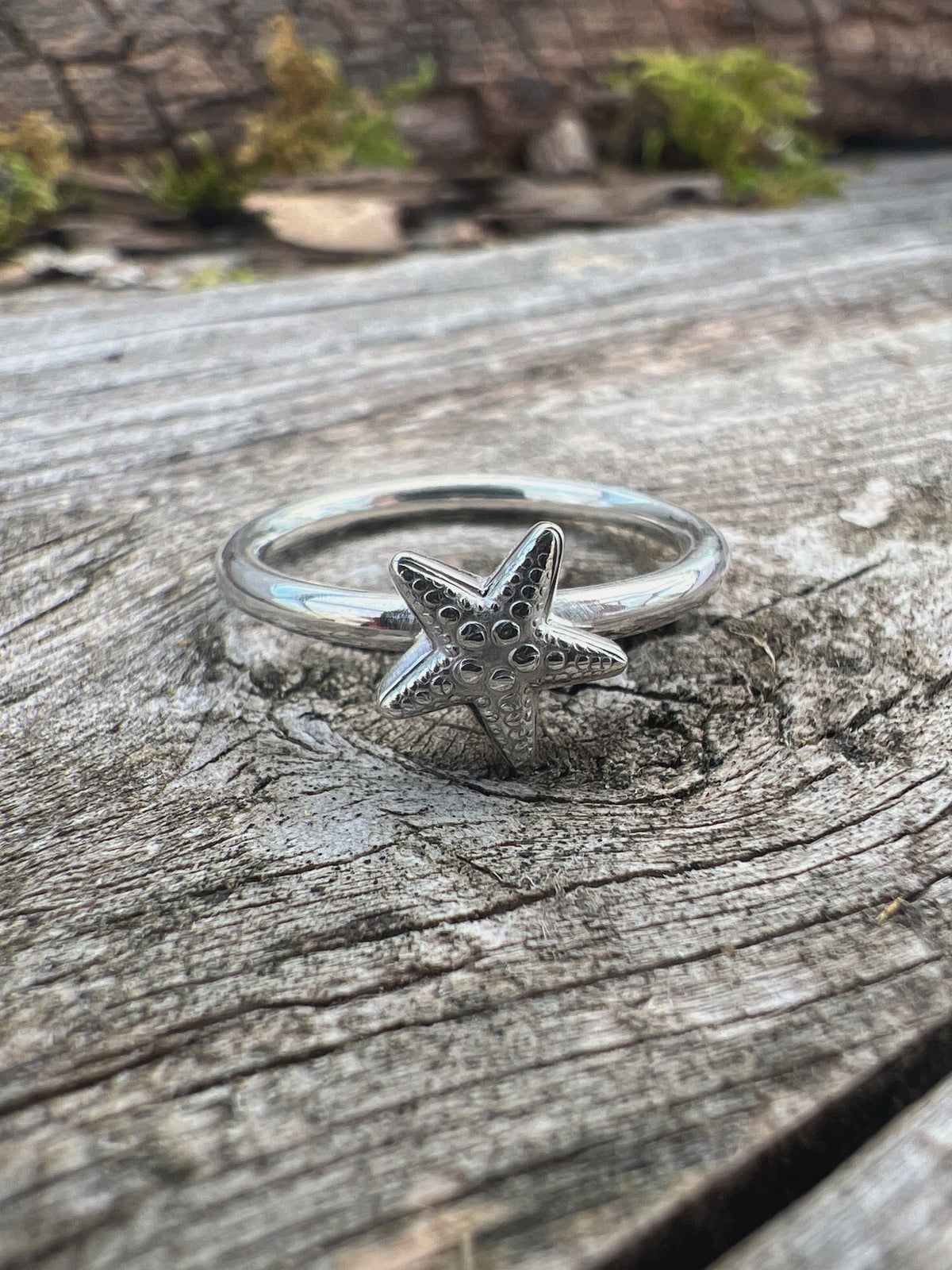 Handmade sterling silver small starfish ring on driftwood, front view showing the starfish detail