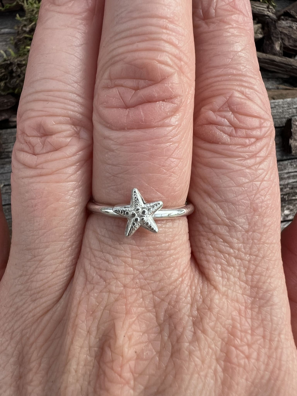 Recycled sterling silver small starfish ring worn on a finger, showing scale and the coastal starfish motif