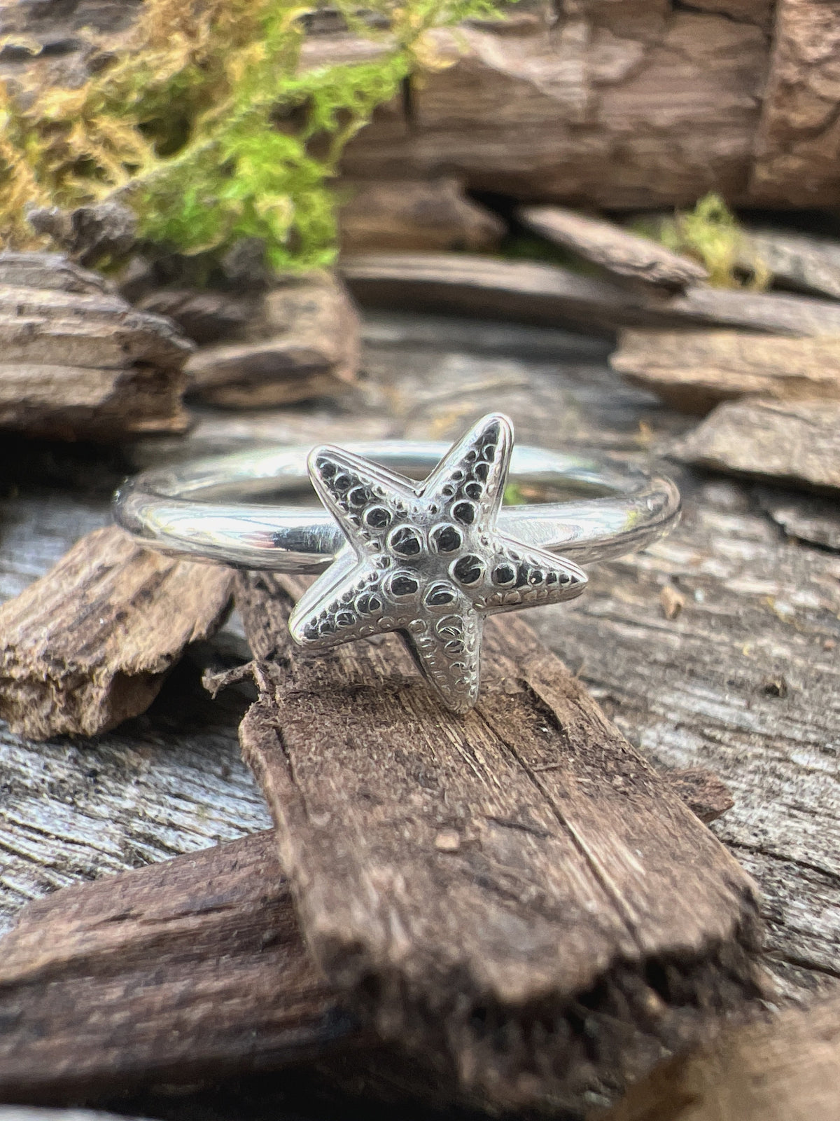 Close-up of a handmade sterling silver small starfish ring on driftwood, highlighting the detailed starfish texture