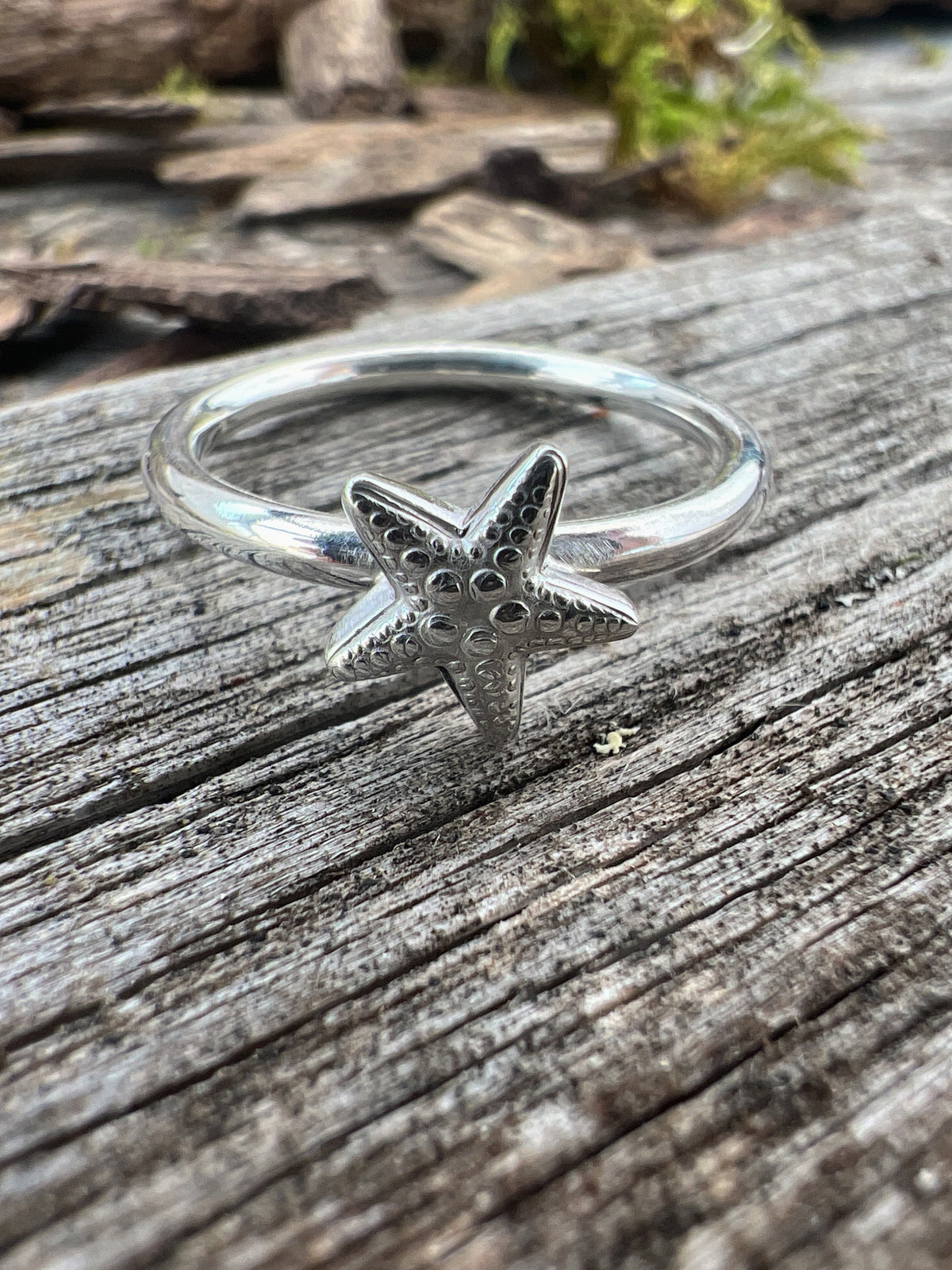 Recycled sterling silver small starfish ring on weathered driftwood, showing the 3D starfish motif on a plain band
