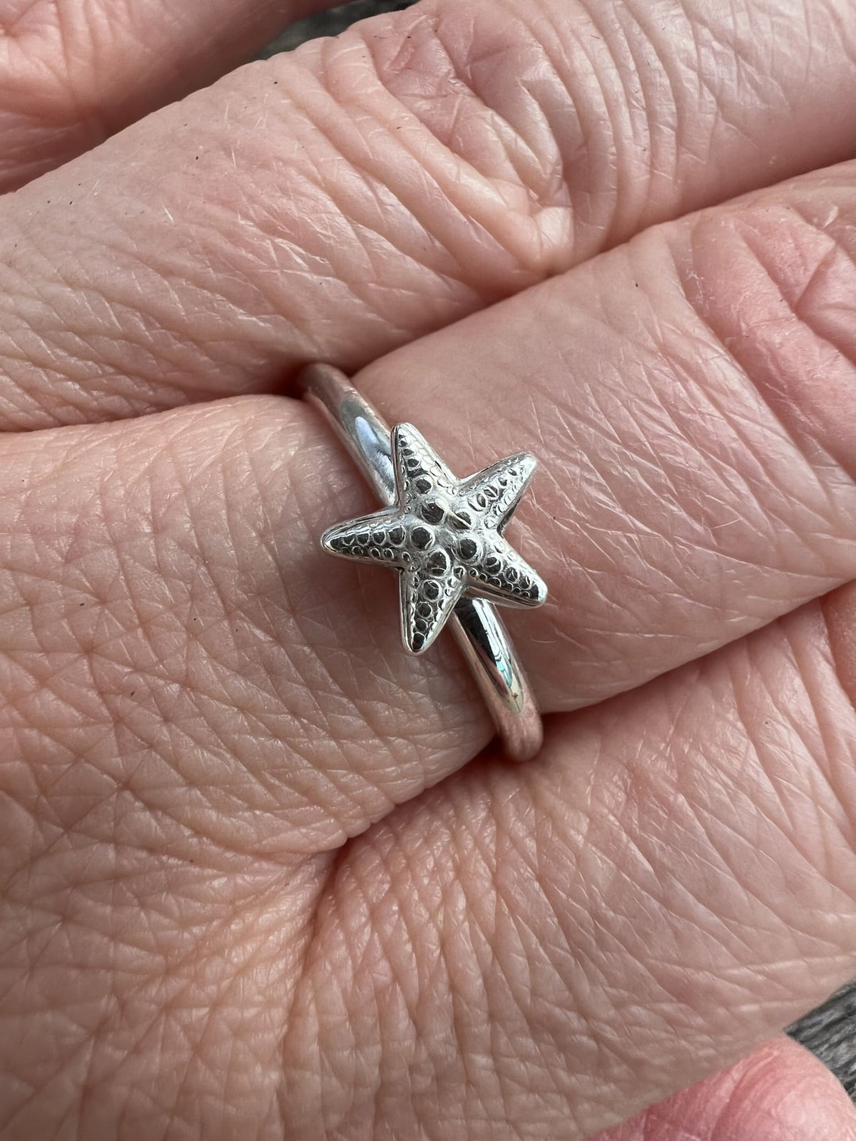 Sterling silver small starfish ring worn on hand, showing the scale of the starfish on the fine band