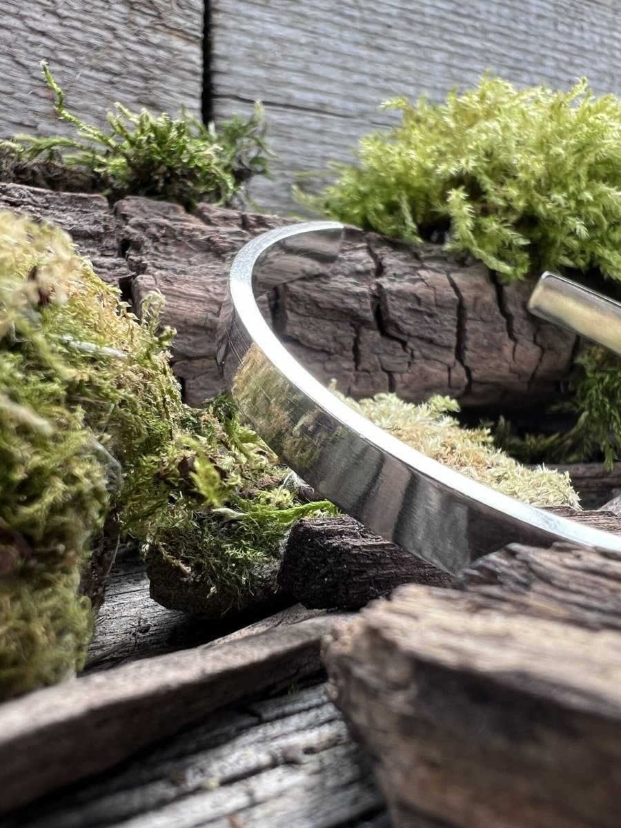 Handmade sterling silver Solstice sleek torque bangle on weathered wood with moss, photographed from a side angle