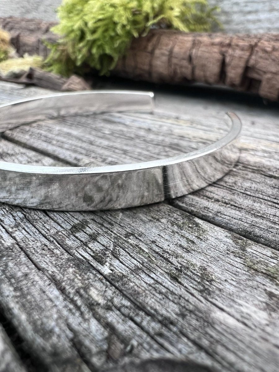 Close-up of a handmade sterling silver Solstice sleek torque bangle on weathered wood, showing the polished finish
