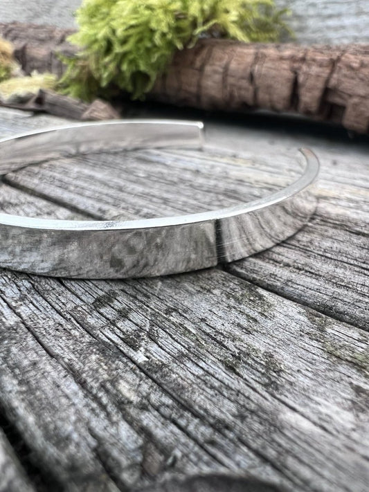 Close-up of a handmade sterling silver Solstice sleek torque bangle on weathered wood, showing the polished finish
