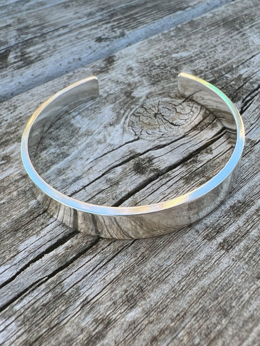 Recycled sterling silver Solstice sleek torque bangle on weathered wood, showing the smooth polished open band