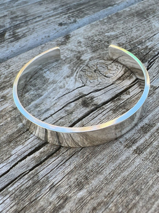 Recycled sterling silver Solstice sleek torque bangle on weathered wood, showing the smooth polished open band