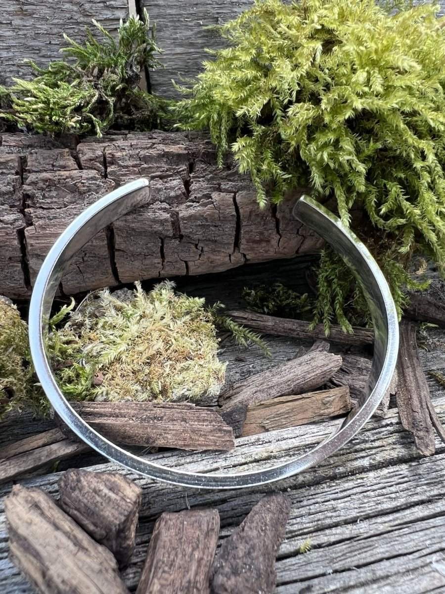 Recycled sterling silver Solstice sleek torque bangle styled in a circular position on mossy weathered wood