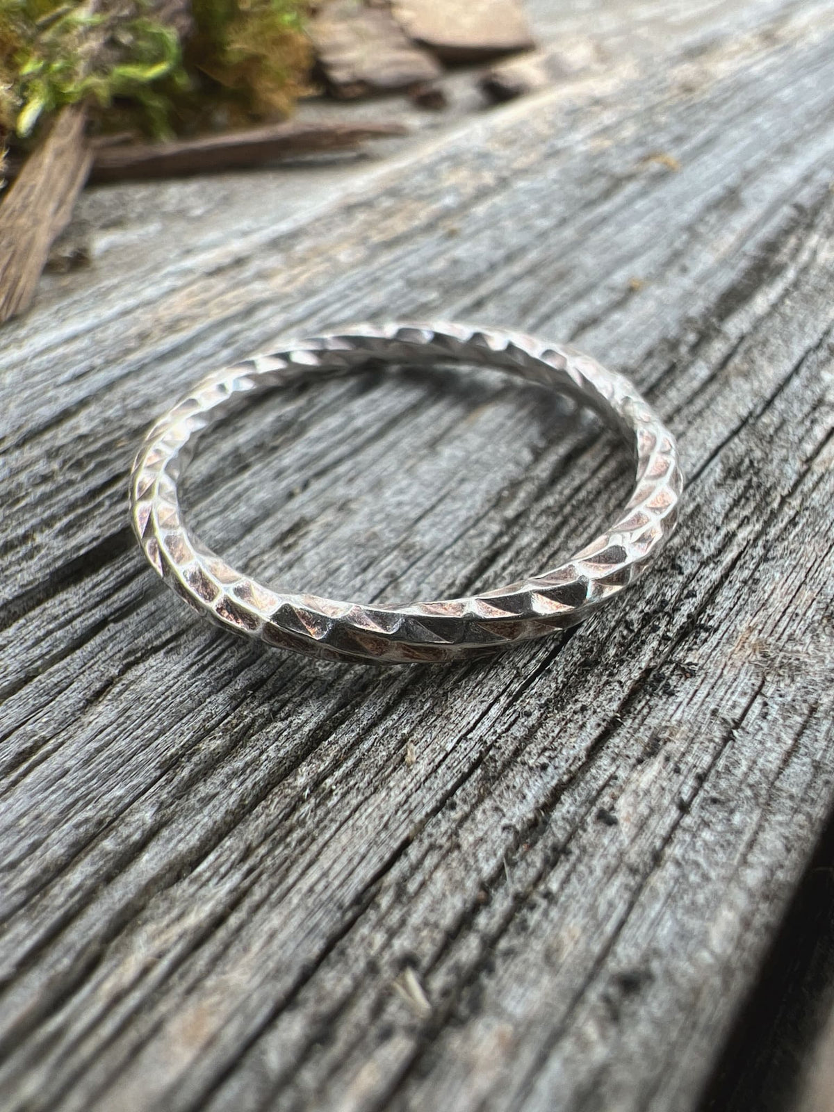 Handmade sterling silver sparkle cut ring on driftwood, front angle showing the faceted band width and profile