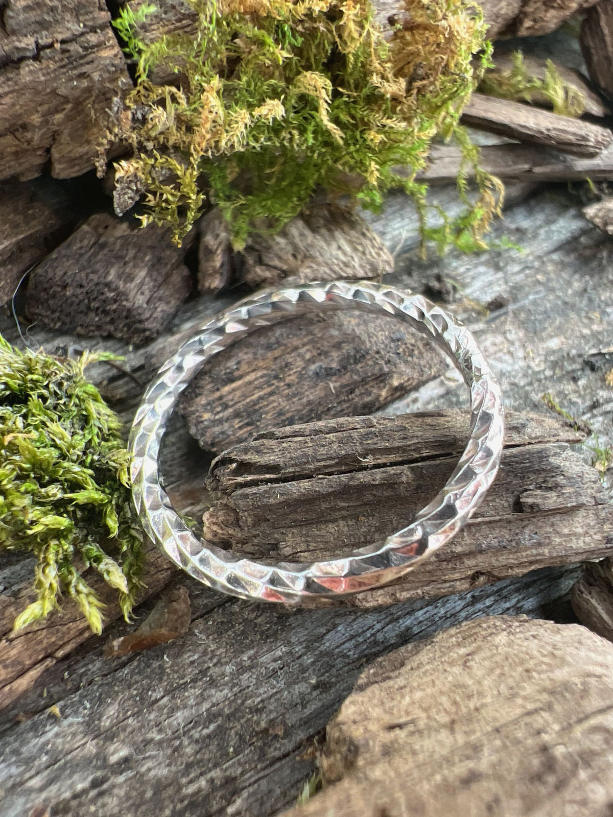 Recycled sterling silver sparkle cut ring on driftwood with moss, showing the faceted band that catches the light