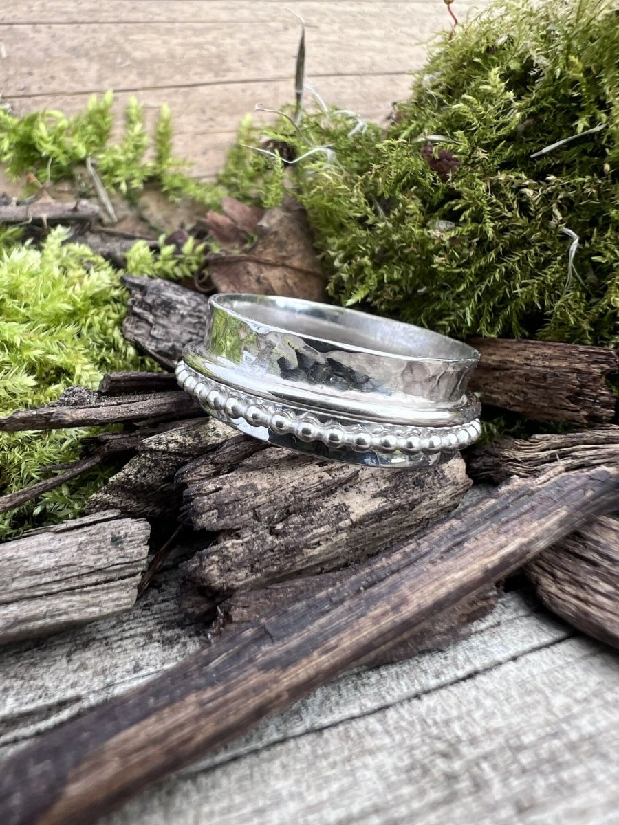 Handmade recycled silver spinner ring with beaded and plain bands on mossy wood chips, viewed from an angle showing band layers