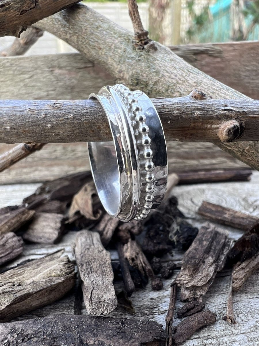 Recycled sterling silver spinner ring with beaded and plain spinning bands hanging on a branch with wood chips, showing the layered multi-band design
