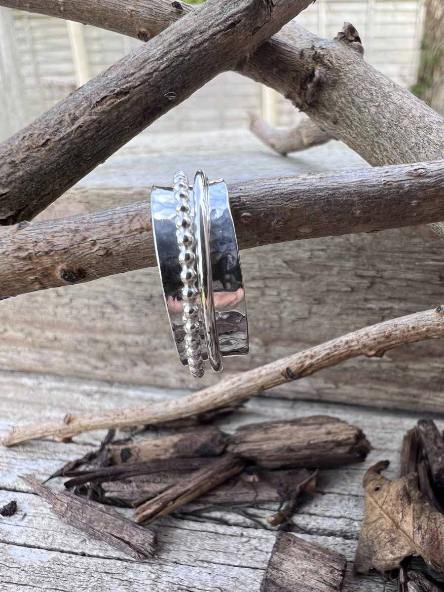 Close-up of a handmade sterling silver spinner ring showing the beaded outer band detail and plain inner band hanging on a branch