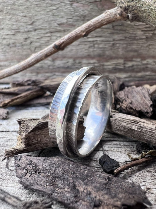 Handmade recycled silver hammered spinner ring on wood chips, photographed from the side to show ring profile