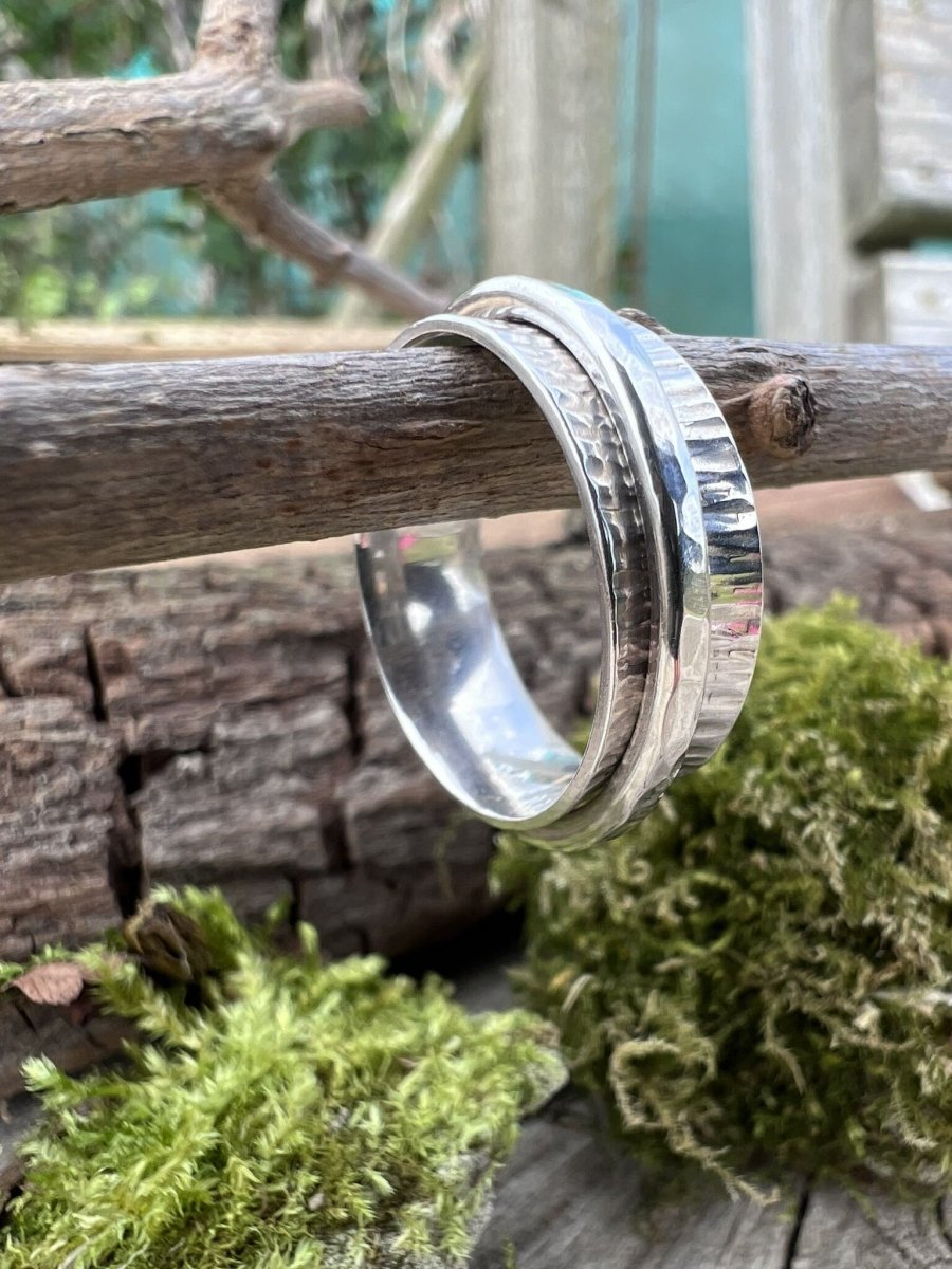 Close-up of a handmade sterling silver hammered spinner ring hanging on branch with moss covered stones, highlighting the beaten metal texture on the outer band
