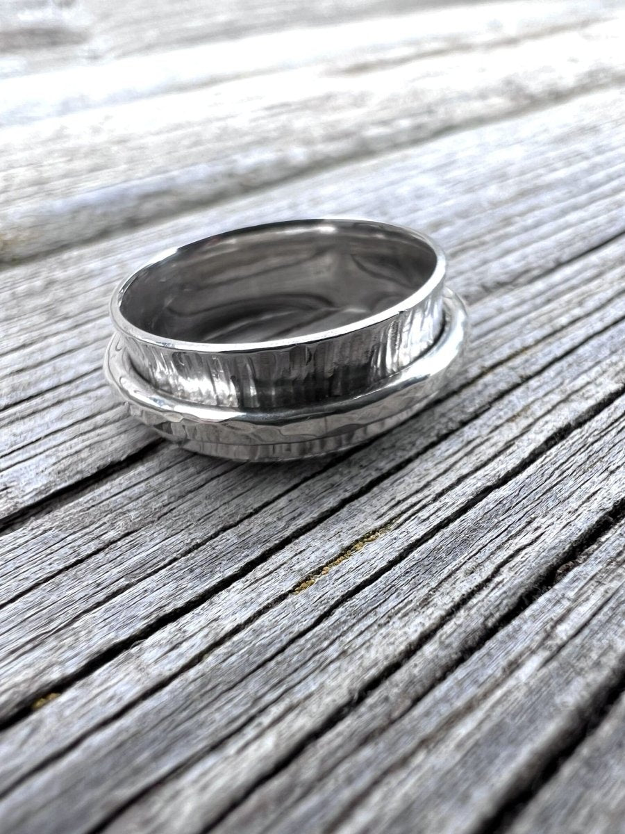 Recycled sterling silver spinner ring with hammered outer band resting on weathered wood, showing the textured spinning element