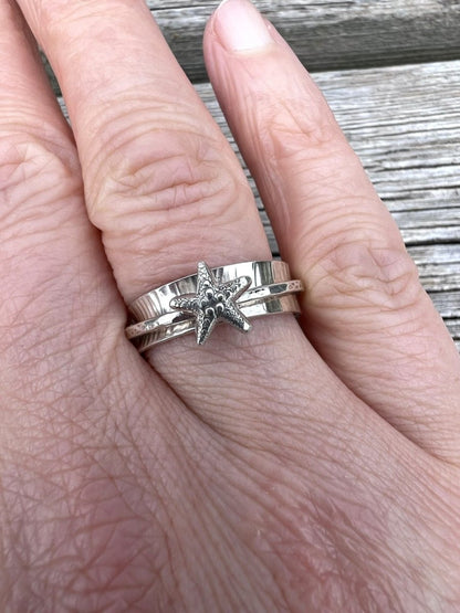 Sterling silver starfish spinner ring worn on a finger, showing scale and the spinning outer band with starfish motif