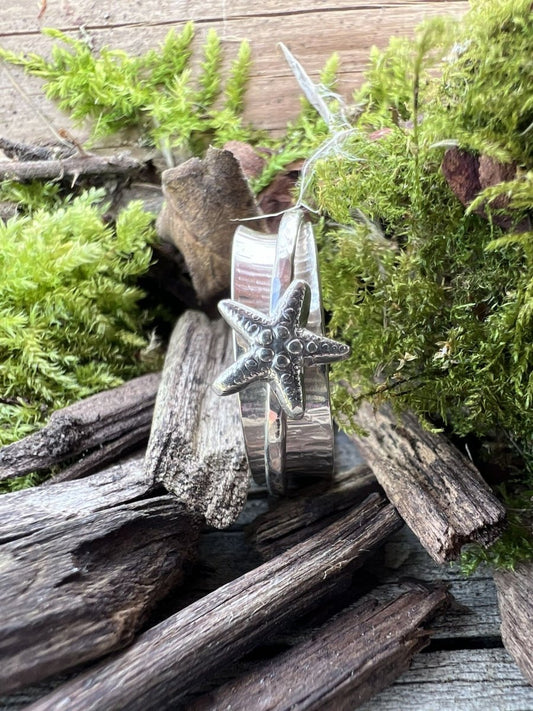 Recycled sterling silver starfish spinner ring styled on wood chips with mossy background, handmade Isle of Wight jewellery