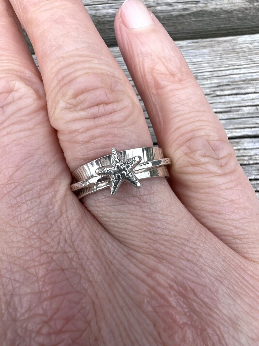 Sterling silver starfish spinner ring worn on a finger, showing scale and the spinning outer band with starfish motif