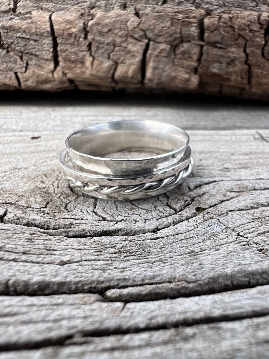Close-up of a handmade sterling silver spinner ring showing the twisted wire and textured band detail on weathered wood