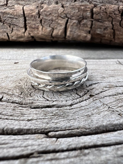 Close-up of a handmade sterling silver spinner ring showing the twisted wire and textured band detail on weathered wood