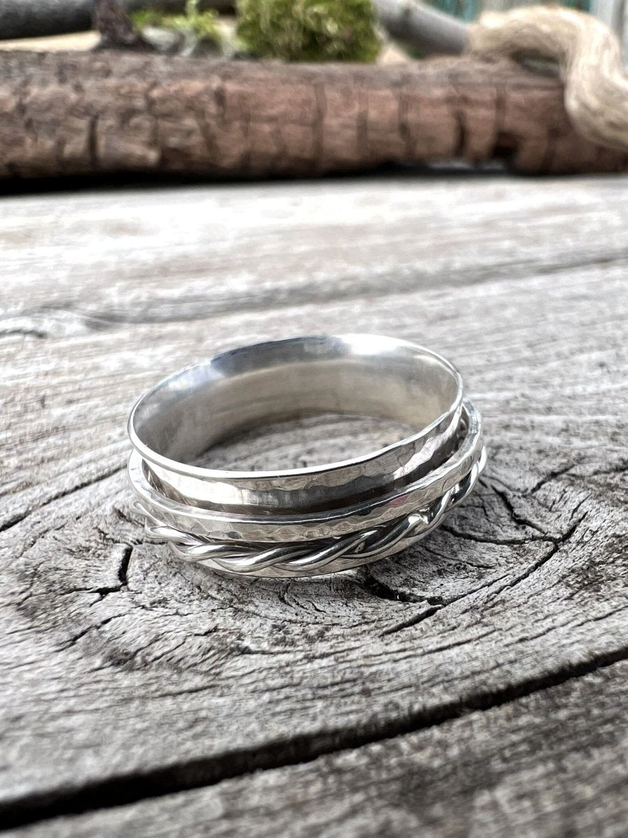 Close-up of a handmade sterling silver spinner ring showing the twisted wire and textured band detail on weathered wood