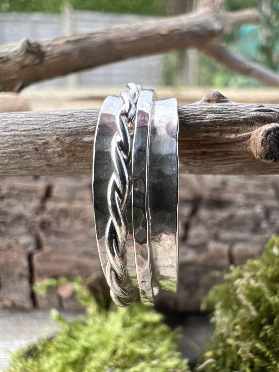 Recycled sterling silver spinner ring with twisted and textured outer bands hanging from a branch with green moss