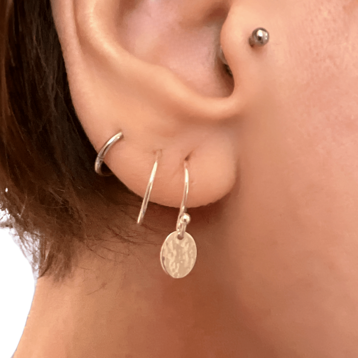 Sterling silver petite textured oval earrings worn in ear, showing the delicate scale of the small hammered oval pendant