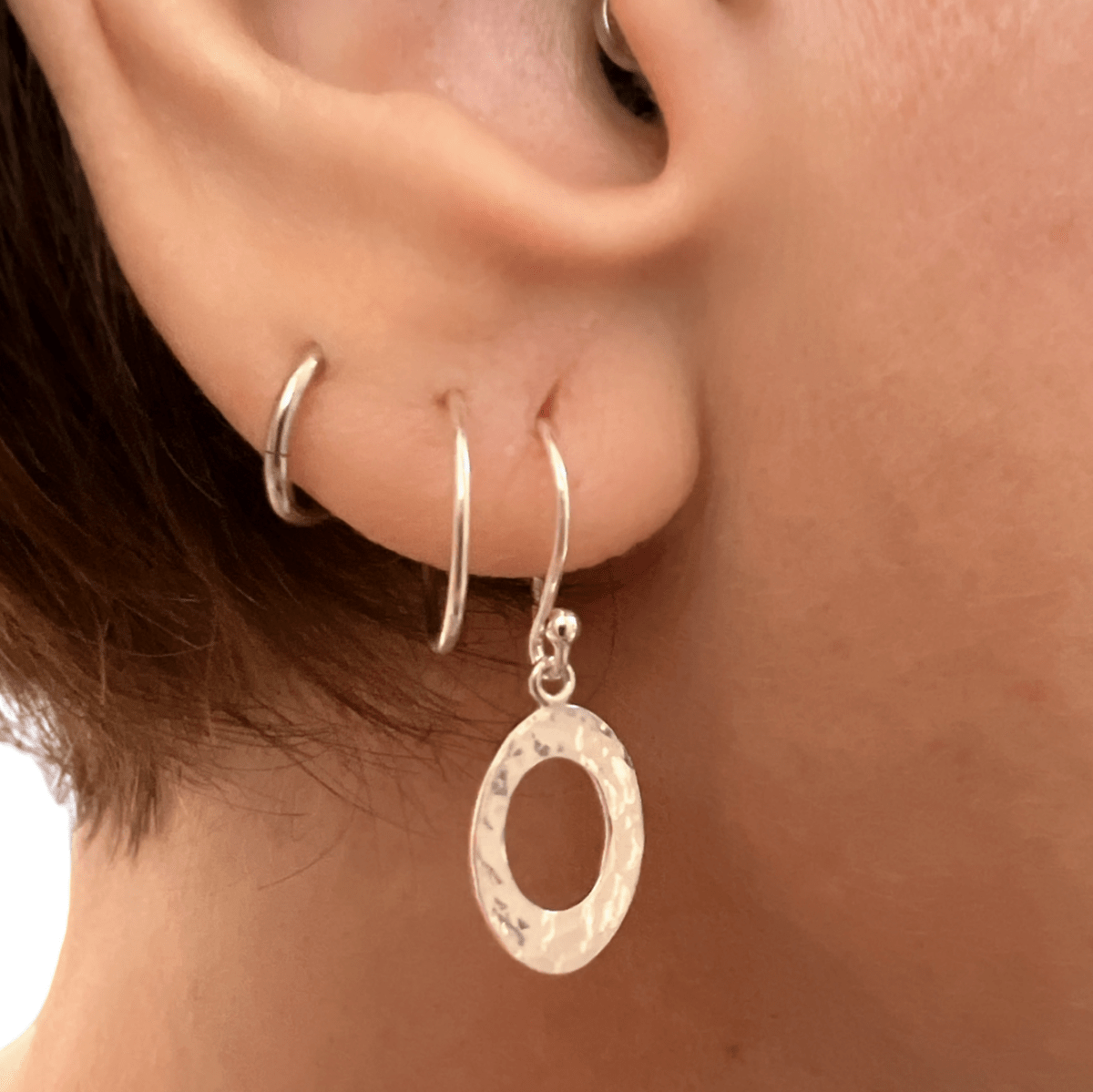 Sterling silver textured oval earrings worn in ear, showing the open oval design and drop length against skin