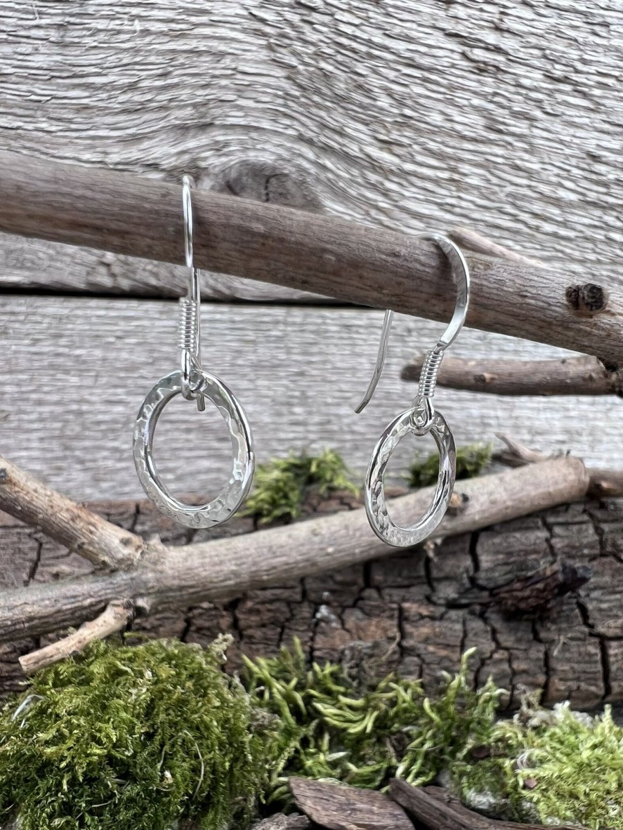 Handmade silver radiant circle earrings photographed from the side on a branch, showing earring length and pendant depth