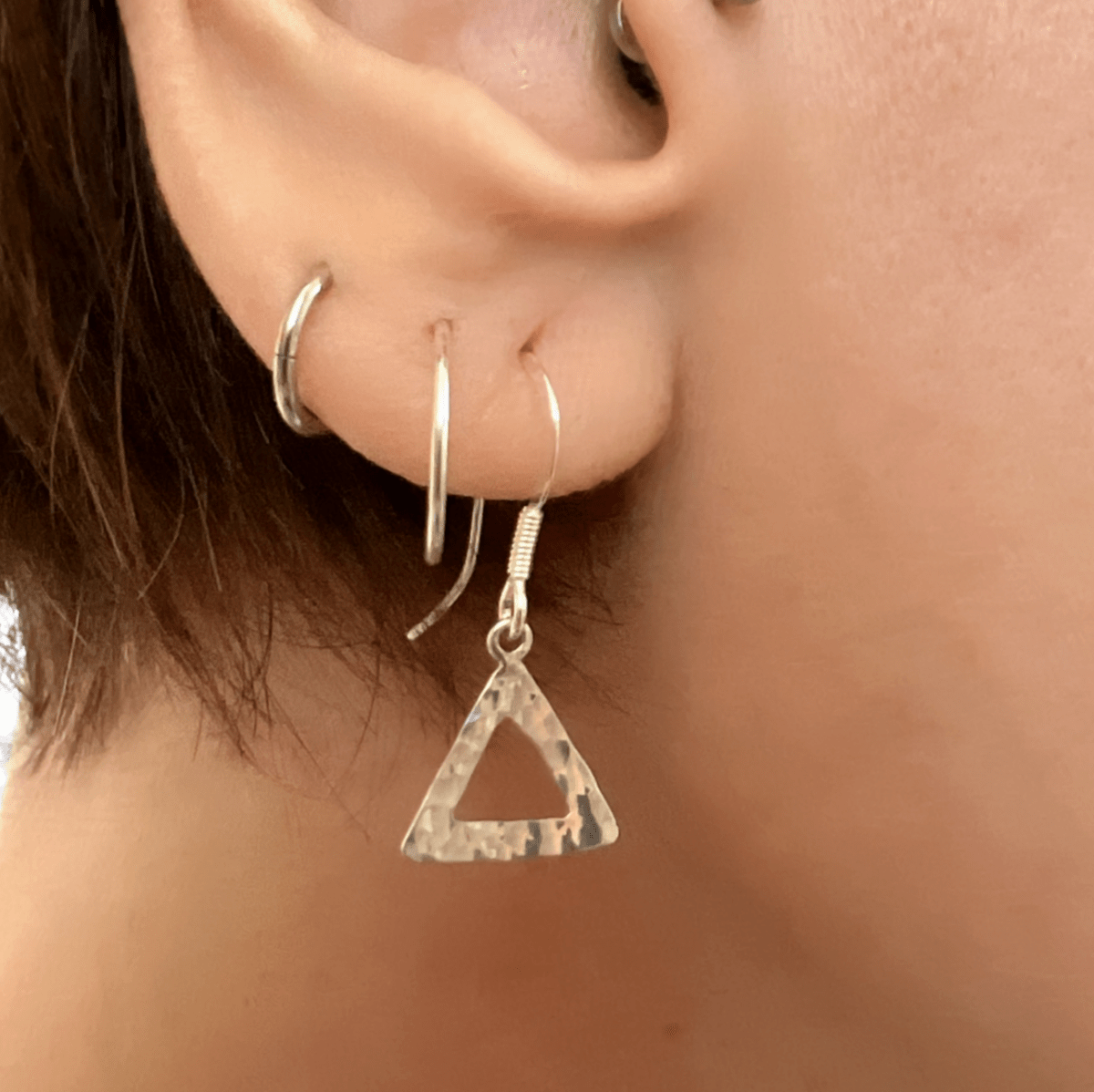 Sterling silver textured triangle earrings worn in ear, showing scale and how the geometric open triangle pendant sits