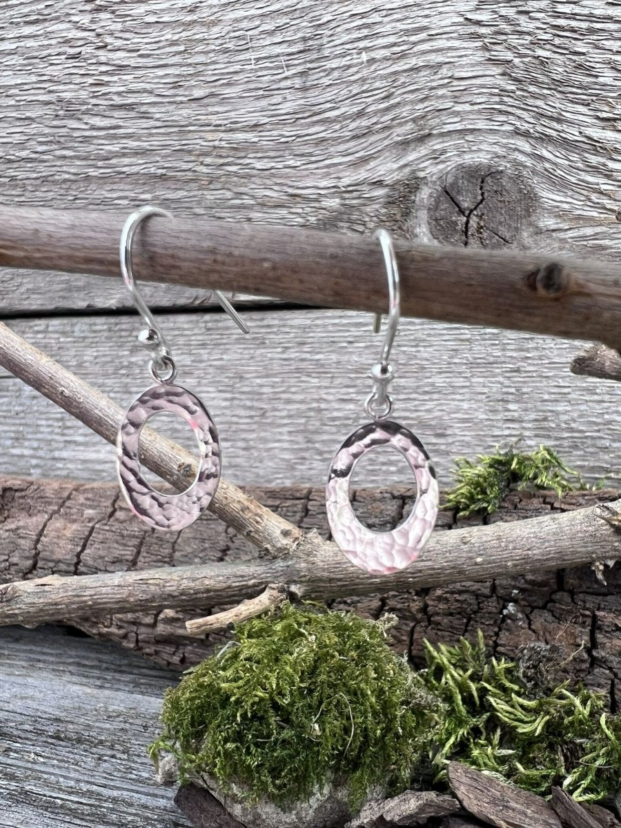 Handmade sterling silver textured oval earrings hanging from a branch showing textured detail with moss and wood chips