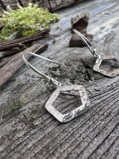 Handmade sterling silver textured pentagon earrings on weathered wood with foliage, angled to show the open frame
