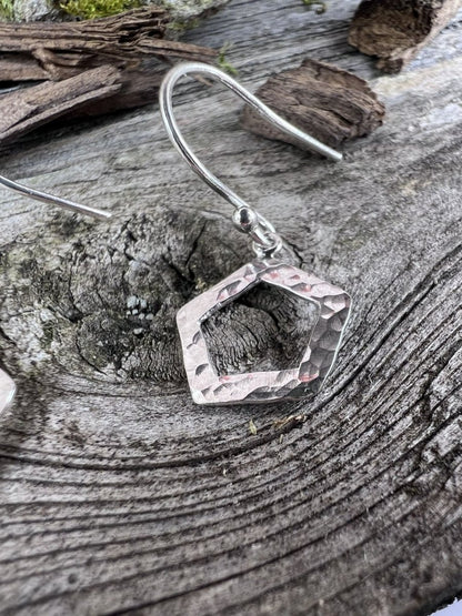 Close-up of handmade sterling silver textured pentagon earrings on weathered wood, highlighting the hammered geometric frame