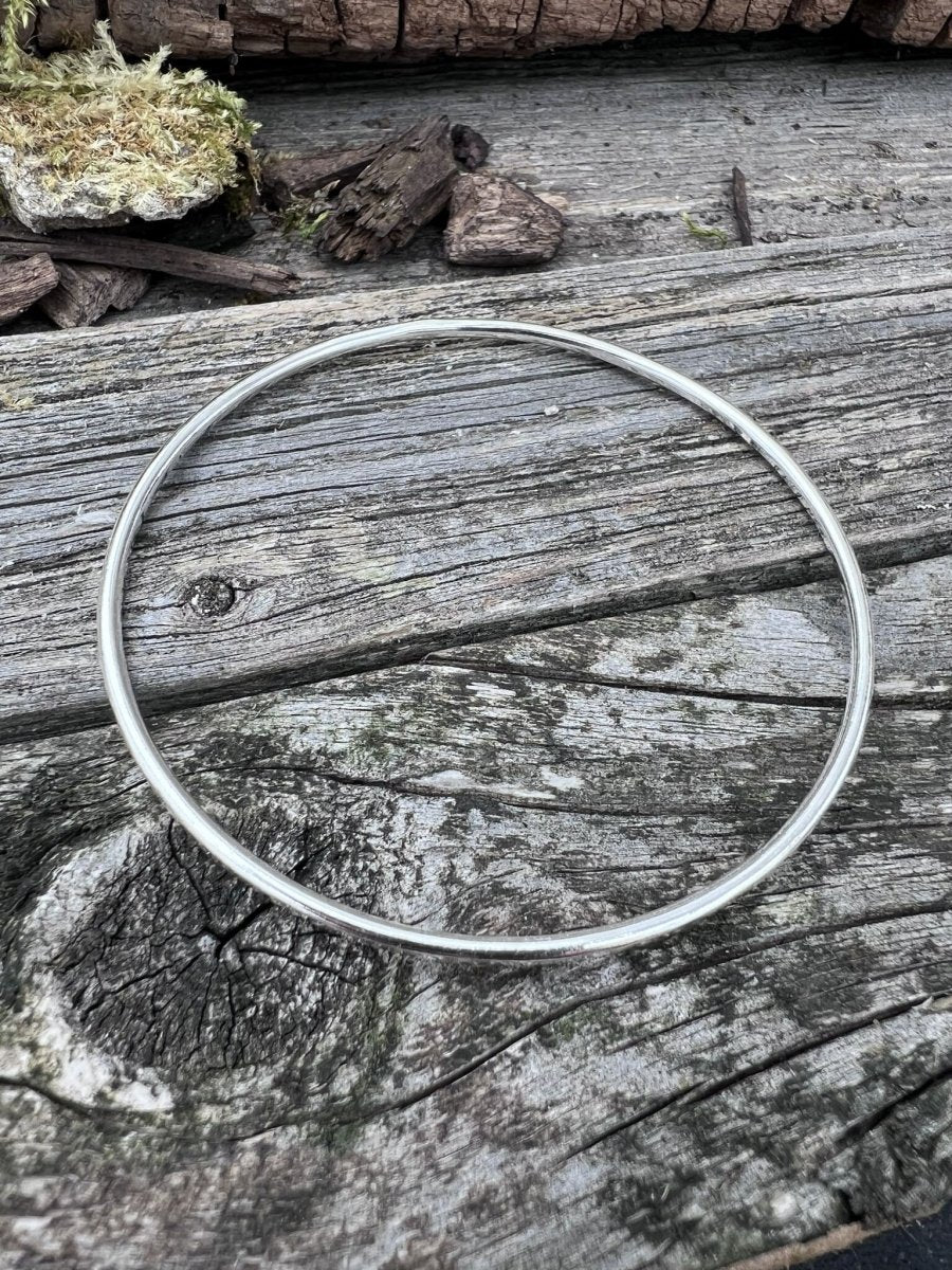 Handmade sterling silver 2mm textured round bangle on wood, photographed from above showing the full circular band