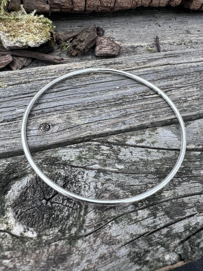 Handmade sterling silver 2mm textured round bangle on wood, photographed from above showing the full circular band