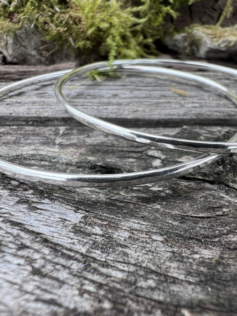 Close-up of handmade sterling silver 2mm textured round bangles on wood, highlighting the fine hammered texture