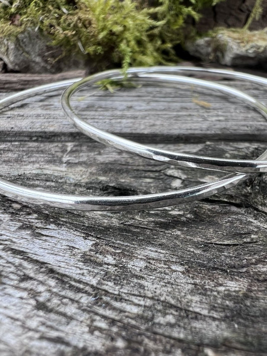 Close-up of handmade sterling silver 2mm textured round bangles on wood, highlighting the fine hammered texture
