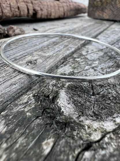 Recycled sterling silver textured round bangle, 2mm, on weathered wood, showing the fine hammered band