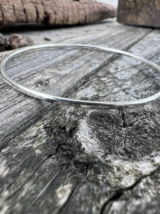 Recycled sterling silver textured round bangle, 2mm, on weathered wood, showing the fine hammered band