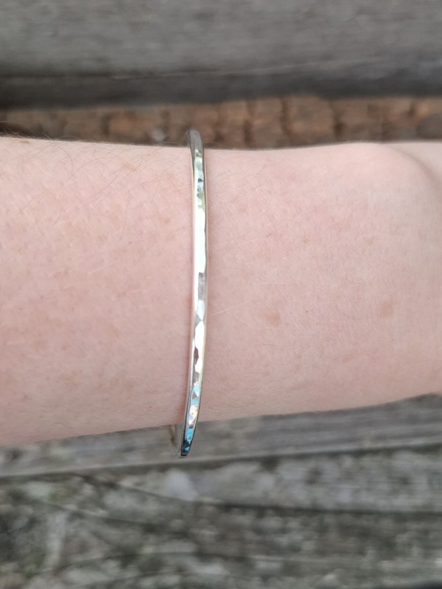 Recycled sterling silver 2mm textured round bangle worn on a wrist, showing the slim band scale and fit