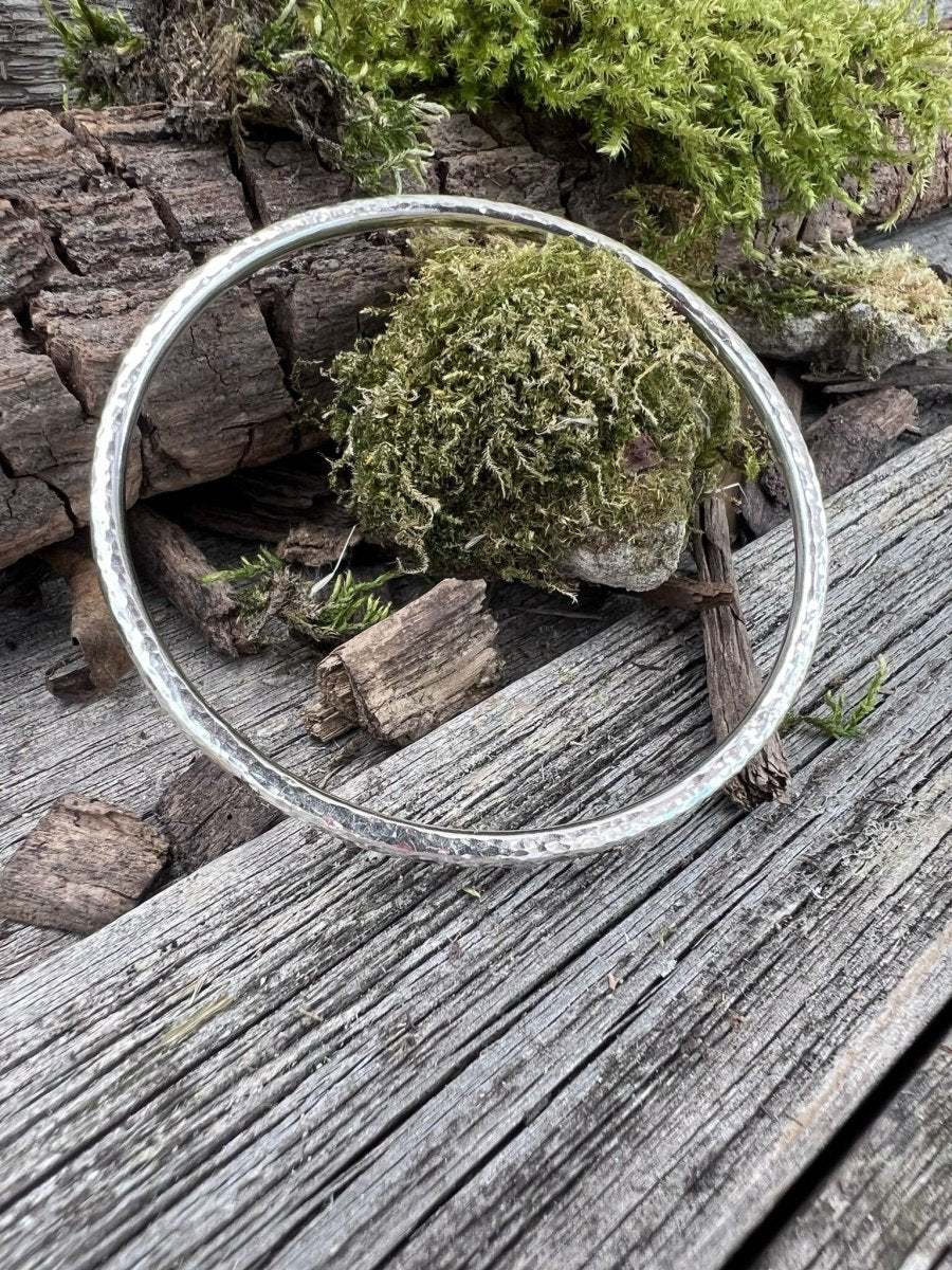 Handmade sterling silver 3.5mm textured round bangle on wood with moss, photographed from above