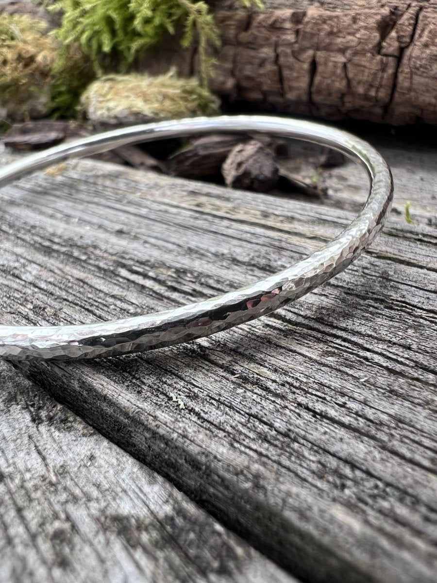 Recycled sterling silver 3.5mm textured round bangle lying flat on weathered wood with mossy background