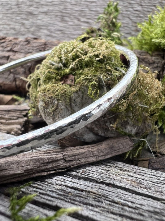 Close-up of a handmade sterling silver 3.5mm textured round bangle on mossy wood, highlighting the hammered texture