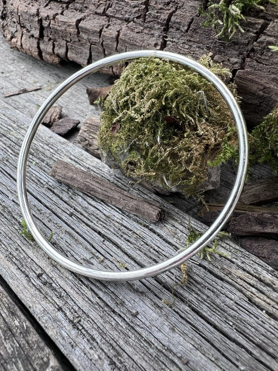 Handmade sterling silver 3mm textured round bangle on wood with moss, photographed from alternative angle