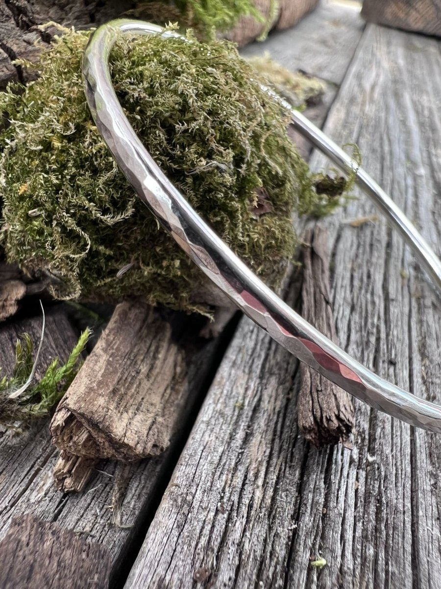 Close-up of a handmade sterling silver 3mm textured round bangle on mossy wood, highlighting the hammered texture