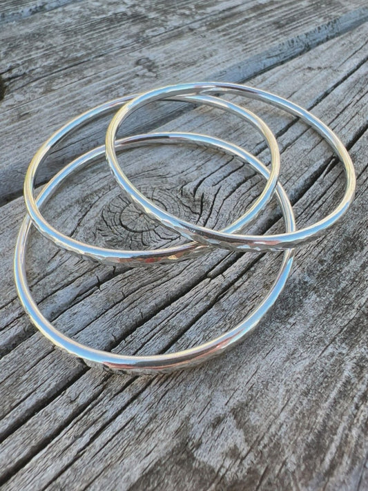 Recycled sterling silver textured round bangles, 3mm, on weathered wood, showing three hammered bands together