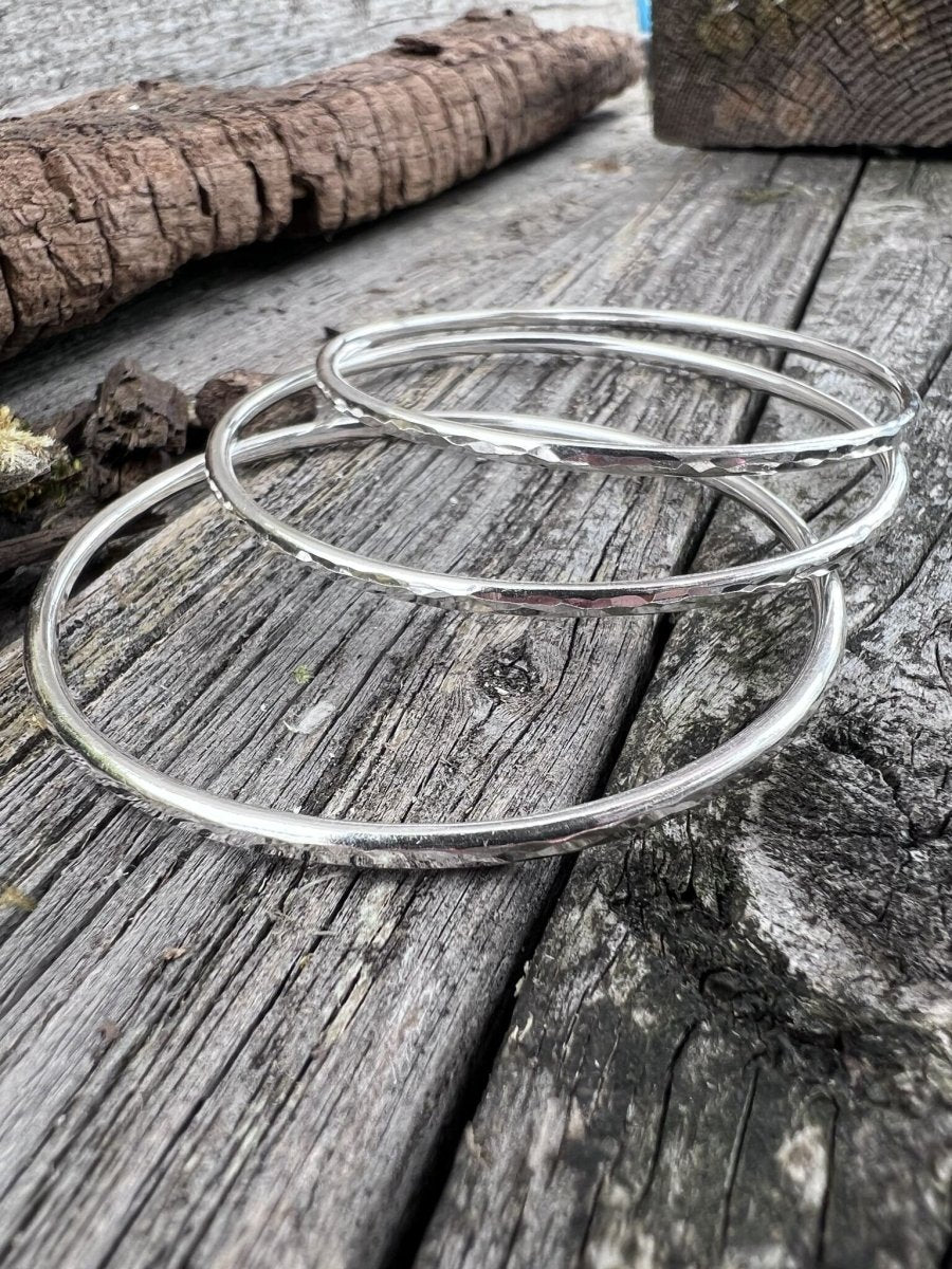 Multiple recycled sterling silver 3mm textured round bangles styled together on weathered wood